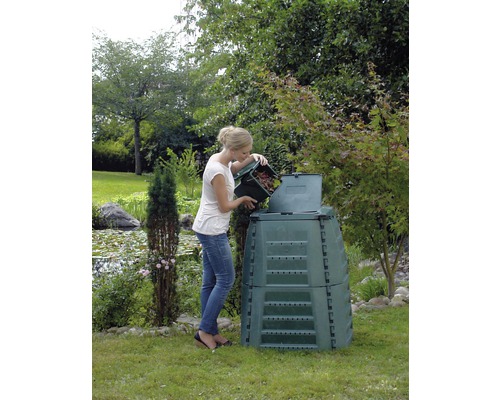 Une femme vide un récipient de déchets de jardin dans un composteur dans le jardin.