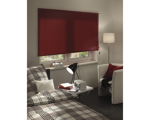 Chambre avec store plissé à la fenêtre, lit et fauteuil.