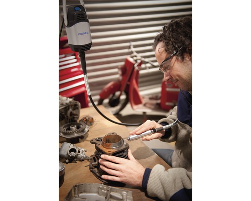 Un homme utilise un outil multifonction Dremel sur un bloc moteur sur un établi.