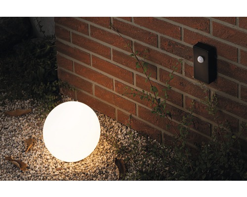 Scène avec un luminaire extérieur rond et un détecteur de mouvement sur un mur de briques