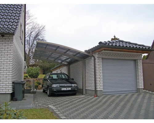 Carport et garage en pierre avec allée pavée et voiture garée