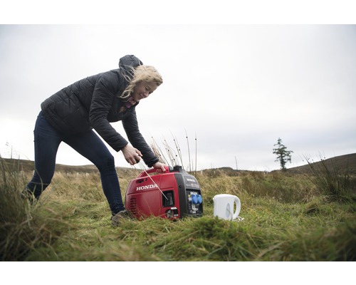 Eine Frau startet einen roten Honda Generator im Freien neben einem Wasserkocher