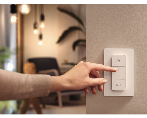 Une main actionne un variateur d'intensité Philips Hue sur le mur.
