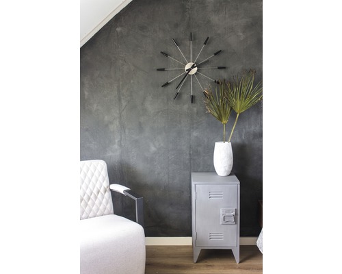 Innenaufnahme eines Raumes mit Sessel, Uhr, Vase mit Pflanzen und Metallschrank