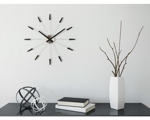 Dekorative Szene mit Wanduhr, Vase, Zweigen, Büchern und Zierkugeln auf einem Tisch.