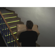 Une personne monte un paquet dans un escalier équipé de marquages de sécurité.