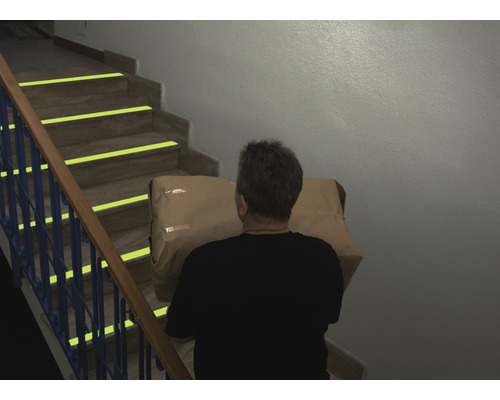 Une personne monte un paquet dans un escalier équipé de marquages de sécurité.