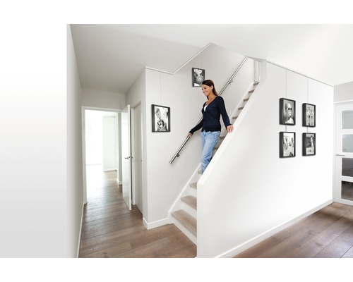 Helles Treppenhaus mit Frau auf der Treppe und aufgehängten Bilderrahmen
