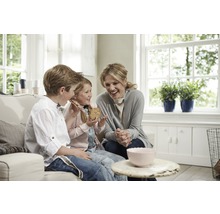 Une femme et deux enfants sont assis sur un canapé et mangent des biscuits dans un salon lumineux et accueillant.