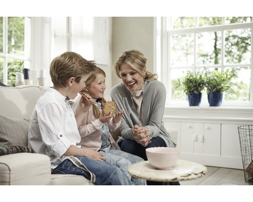 Eine Frau und zwei Kinder sitzen auf einem Sofa und essen Kekse in einem hellen, freundlichen Wohnzimmer.