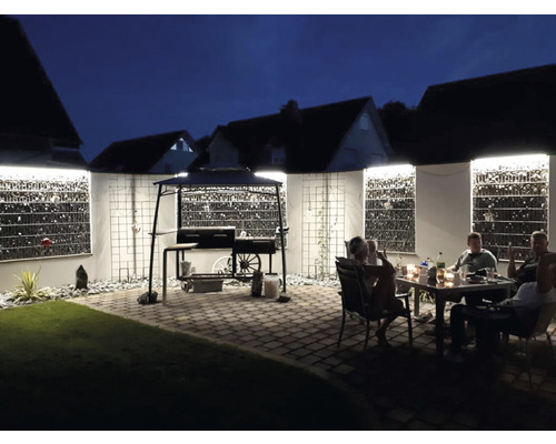 Scène de jardin nocturne avec barbecue, murs en gabions et personnes assises