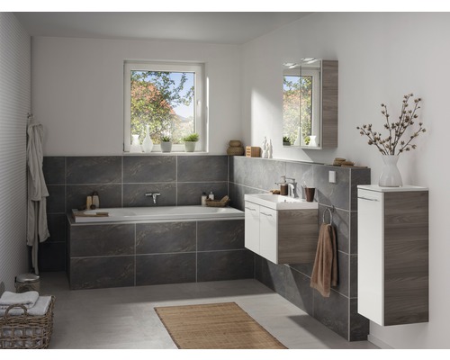 Salle de bains avec baignoire, lavabo, armoire de toilette et armoire haute en décor bois clair et foncé et carrelage gris.