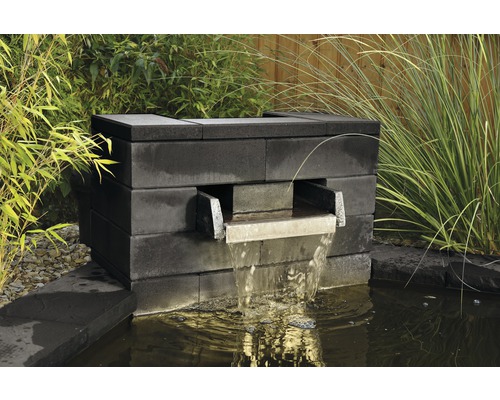 Gartenbrunnen aus Steinblöcken mit Wasserauslauf in einem Gartenteich