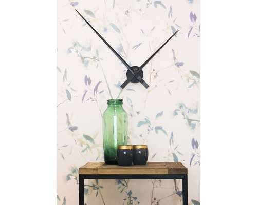 Décoration avec horloge murale, vase en verre et bougies sur une table en bois devant un papier peint floral