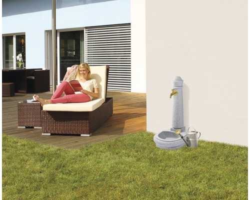 Scène de jardin avec chaise longue, fontaine et femme lisant