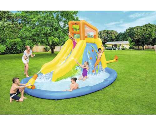 Aufblasbarer Wasserpark mit Rutschen, Kletterwand und Planschbecken im Garten mit spielenden Kindern.