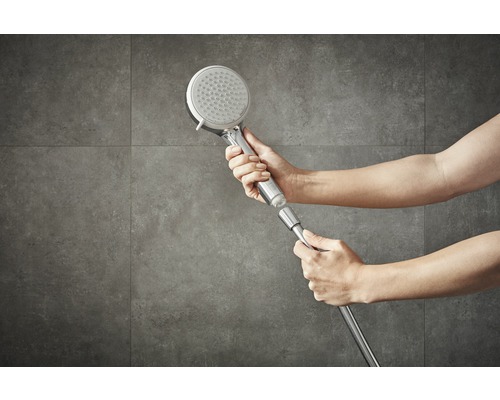 Une personne fixe une pomme de douche sur un flexible de douche.