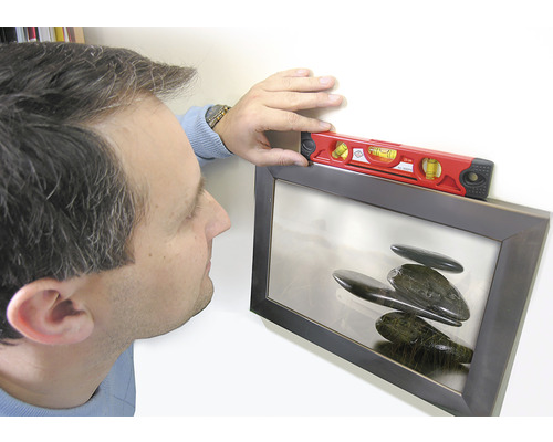 Eine Person richtet ein gerahmtes Bild mit einer Wasserwaage aus.