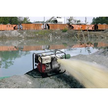 Pompe à eau en marche à côté d''un plan d''eau avec des wagons de train en arrière-plan.