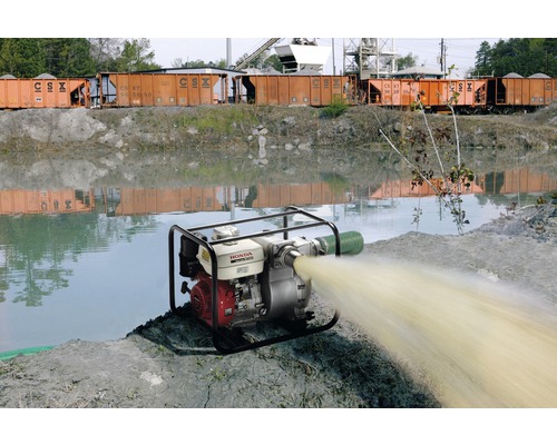 Pompe à eau en marche à côté d''un plan d''eau avec des wagons de train en arrière-plan.