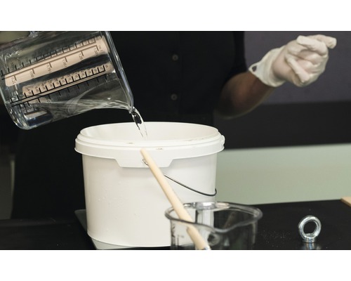 De l''eau est versée d''un verre doseur dans un seau.
