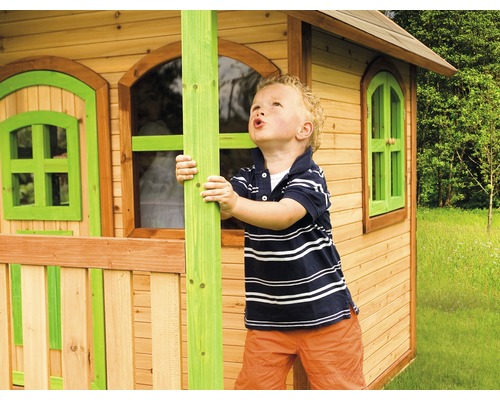 Junge spielt vor einem Holzspielhaus mit Fenstern