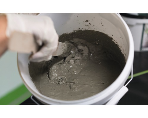 Un seau de mortier gâché est mélangé avec une spatule.