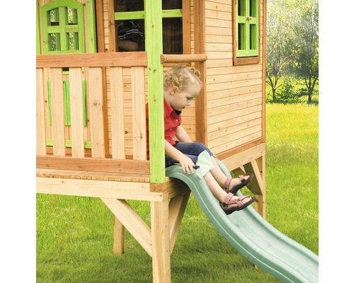 Kind auf einer Rutsche eines Holzspielhauses im Garten.