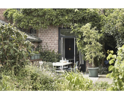 Ein Garten mit Ziegelmauer, begrünt mit Pflanzen und einem Esstisch mit Stühlen.