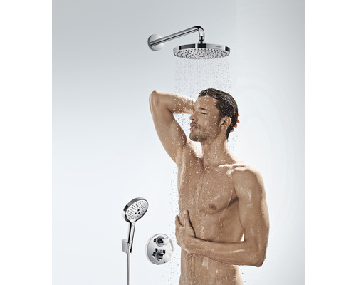 Mann unter einer Kopfbrause mit Handbrause und Thermostatbatterie im Badezimmer