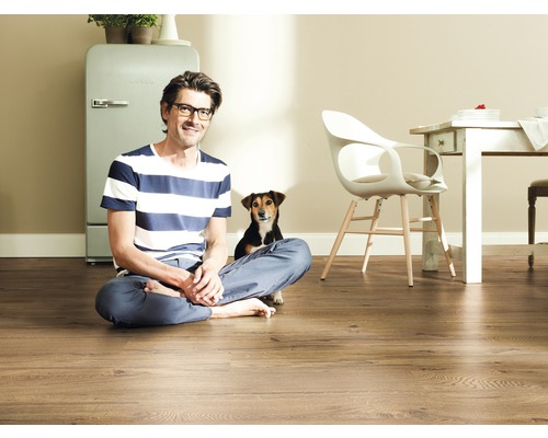 Mann sitzt mit Hund auf Holzlaminat in einem hellen Raum