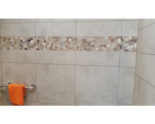 Wandfliesen mit Kieselsteinbordüre in einem Badezimmer.