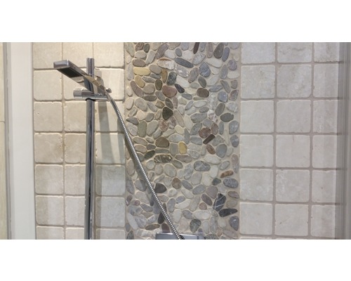 Detailaufnahme eines Duschkopfes vor einem Hintergrund aus Kieselsteinen und Fliesen