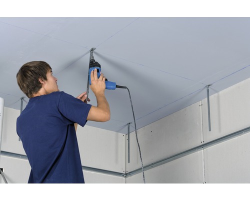 Un homme monte une structure de plafond avec une perceuse