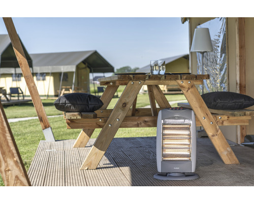 Scène avec une table de pique-nique en bois, des coussins et un chauffage devant des tentes