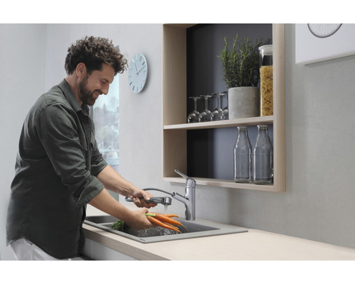 Un homme lave des carottes dans un évier de cuisine avec un robinet extractible.