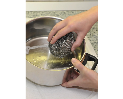 Une personne nettoie une casserole avec une éponge de laine d''acier.