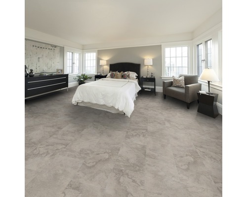 Schlafzimmer mit Bett, Kommode, Sessel und Bodenbelag in Steinoptik