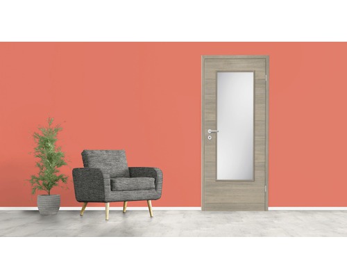 Wohnzimmer mit grauem Polstersessel, Zimmerpflanze und Innentür mit Glaseinsatz.