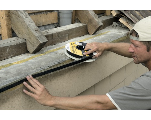 Ein Mann befestigt ein Dichtband an einer Betonwand.