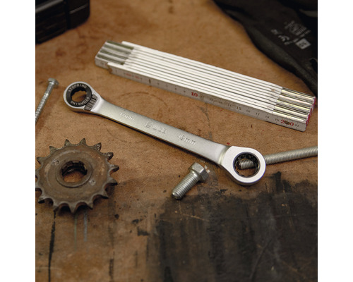 Clé polygonale à cliquet, mètre pliant, vis et roue dentée sur un établi