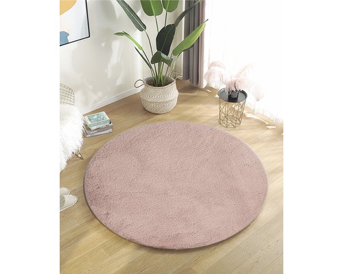 Tapis rond de teinte rose dans un espace de vie lumineux avec une plante en pot et une table d''appoint