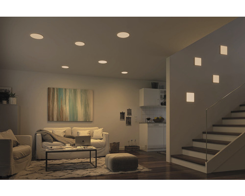 Salon avec spots encastrés au plafond et appliques murales à côté d''un escalier.