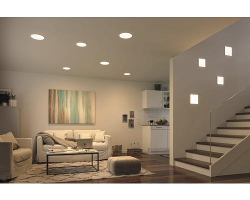 Salon avec spots encastrés au plafond et appliques murales près d''un escalier