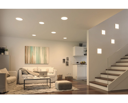 Salon avec spots encastrés au plafond et cage d''escalier avec appliques murales pour une ambiance claire et moderne