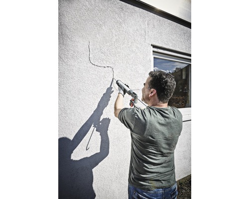 Mann dichtet einen Riss in einer Wand mit einer Dichtpistole ab.