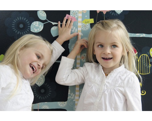 Deux enfants près d''un tableau de croissance devant un papier peint floral