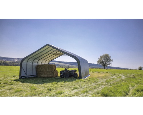 Hangar tubulaire en acier avec bottes de foin et quad dans un pré