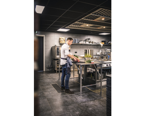 Un cuisinier prépare des plats dans une cuisine professionnelle sur un plan de travail en acier inoxydable.