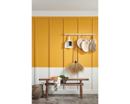 Scène décorative avec balais, pelle, banc et légumes devant un lambris jaune et blanc